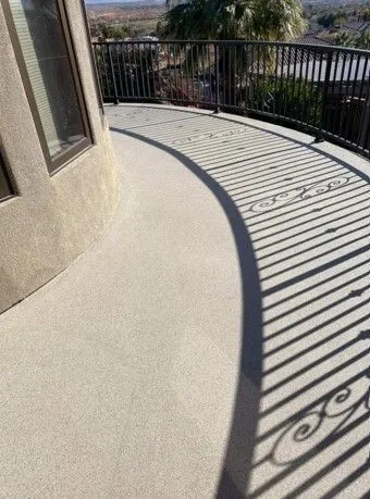 Curved outdoor patio with railing. Sunlight casts a long shadow across the light-colored surface.