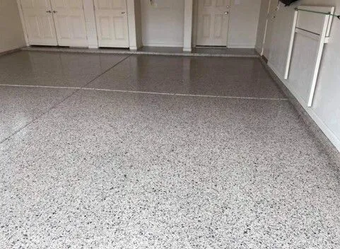 Gray and black flake epoxy garage floor beside white storage cabinets and doors.