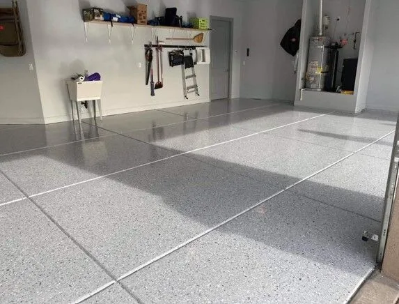 Gray flake epoxy garage floor with saw-cut lines, a wall storage rack, and a water heater.