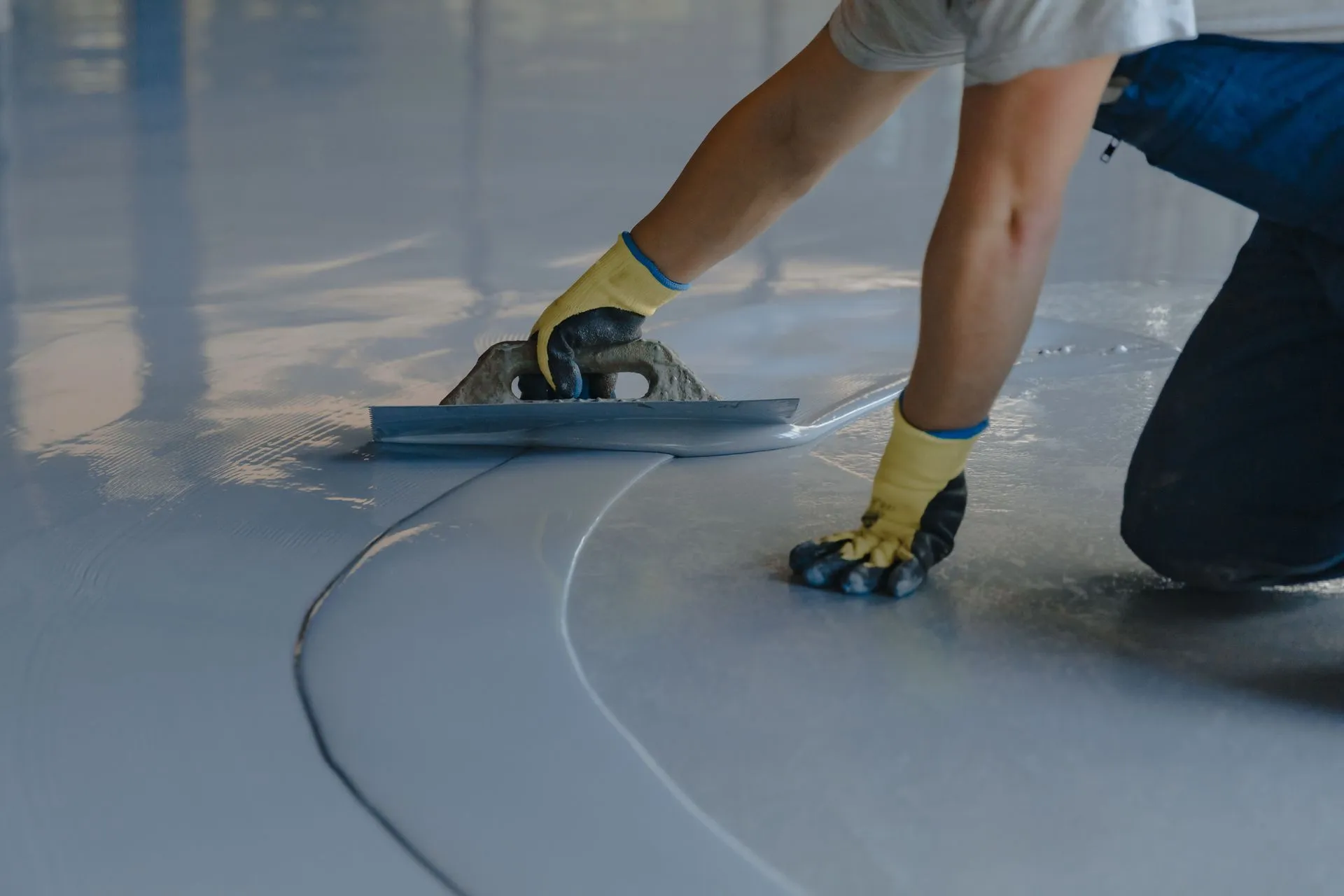 Installer in gloves spreading gray epoxy across a floor with a flat trowel