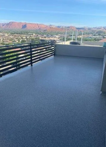 Rooftop deck with dark gray surface, black railing, and distant red rock mountains.