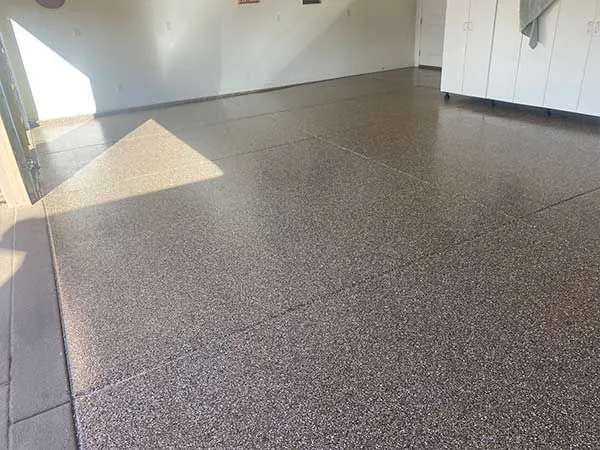 Tan and brown flake epoxy garage floor with sunlight across the saw-cut joints.