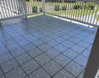 Gray tiled porch with white railing, overlooking a yard.